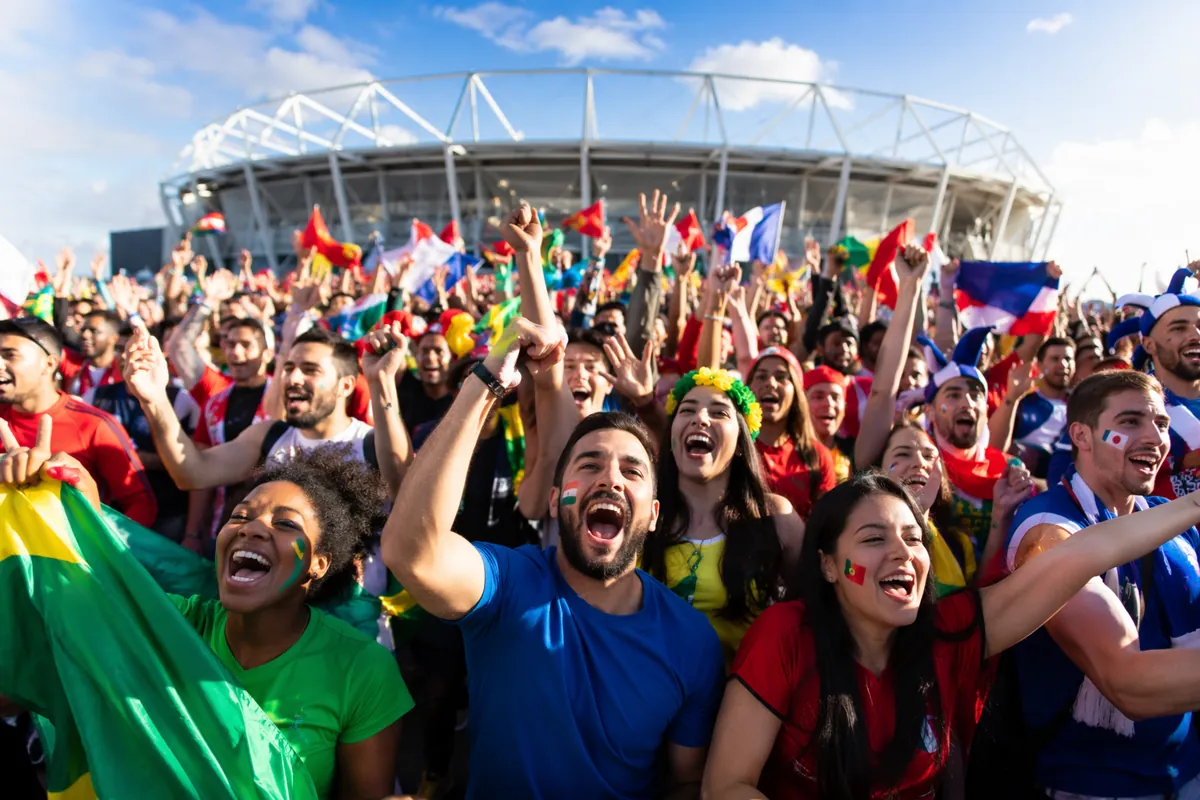 Wide shot of a vibrant outdoor World Cup viewing party with diverse fans cheering, generic